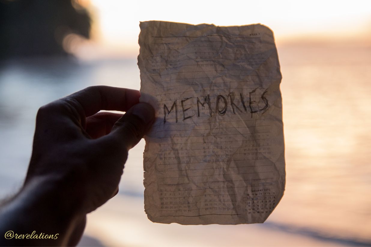 Hand holding up a sheet of crumpled paper that says memories against sunny background