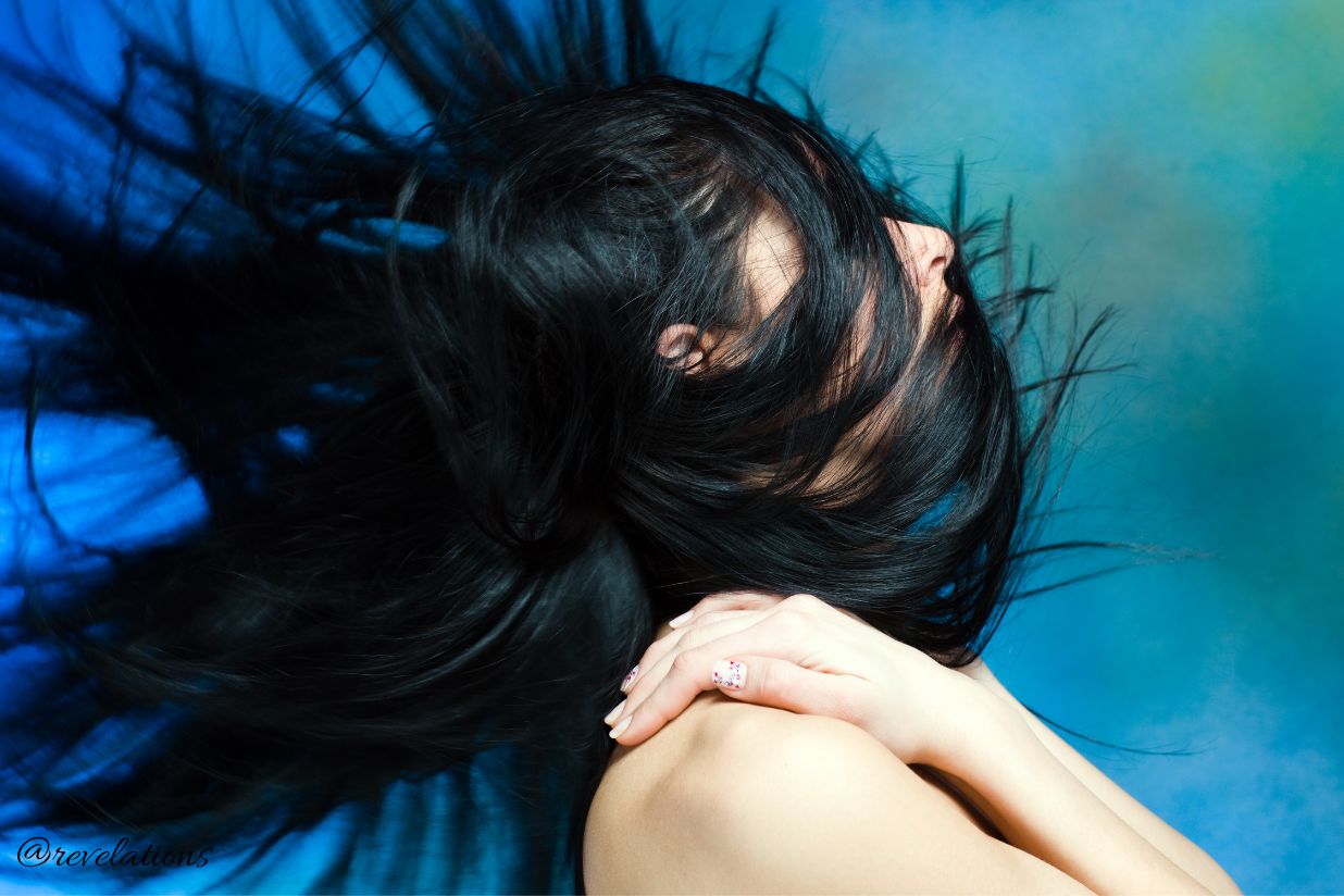 Person with long balck hair wrapped round their head and face and with it flowing out behind them