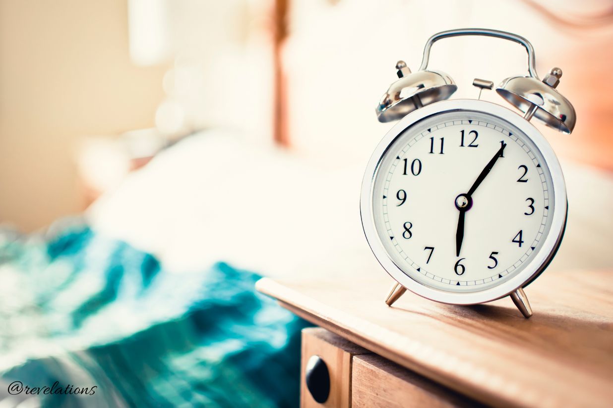 Alarm clock that says 6.05am next to empty bed for post about stay up all night